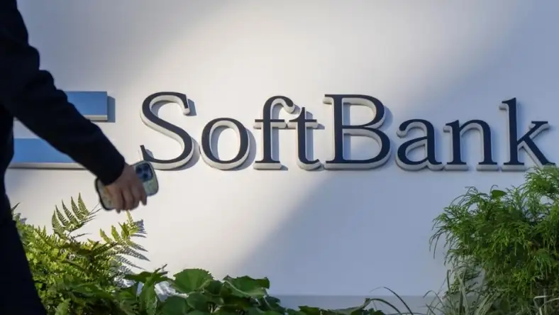 SoftBank logo displayed on an office wall with indoor plants and a person walking past